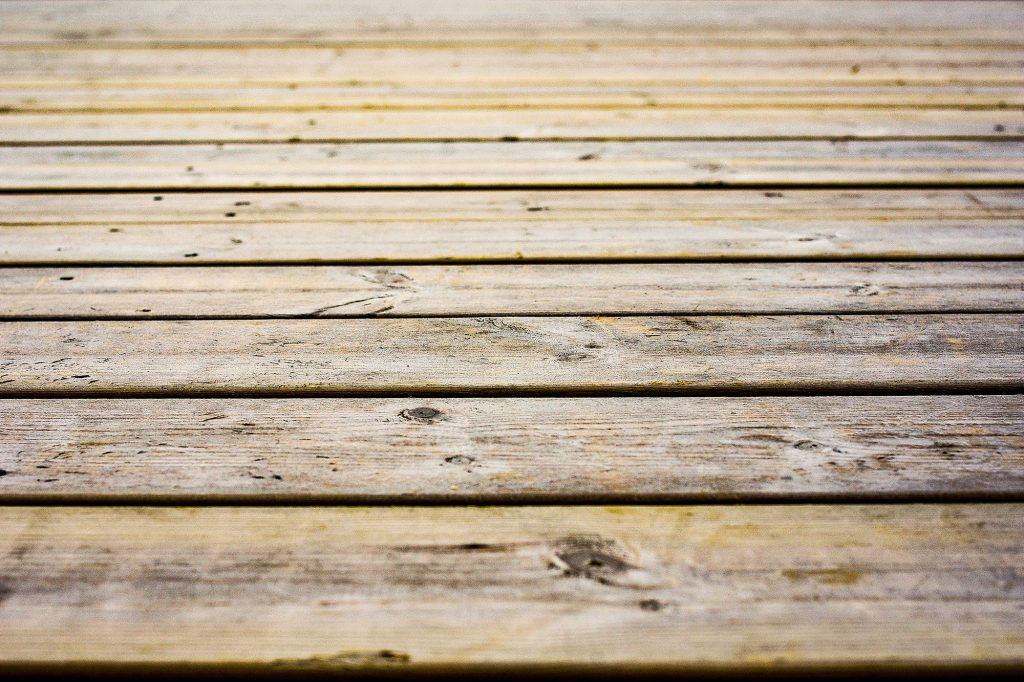 Eine stark in die Jahre gekommene, sichtlich verwitterte Holzterrasse, deren alte Dielen von unzähligen, unschön sichtbaren Schrauben durchzogen sind.